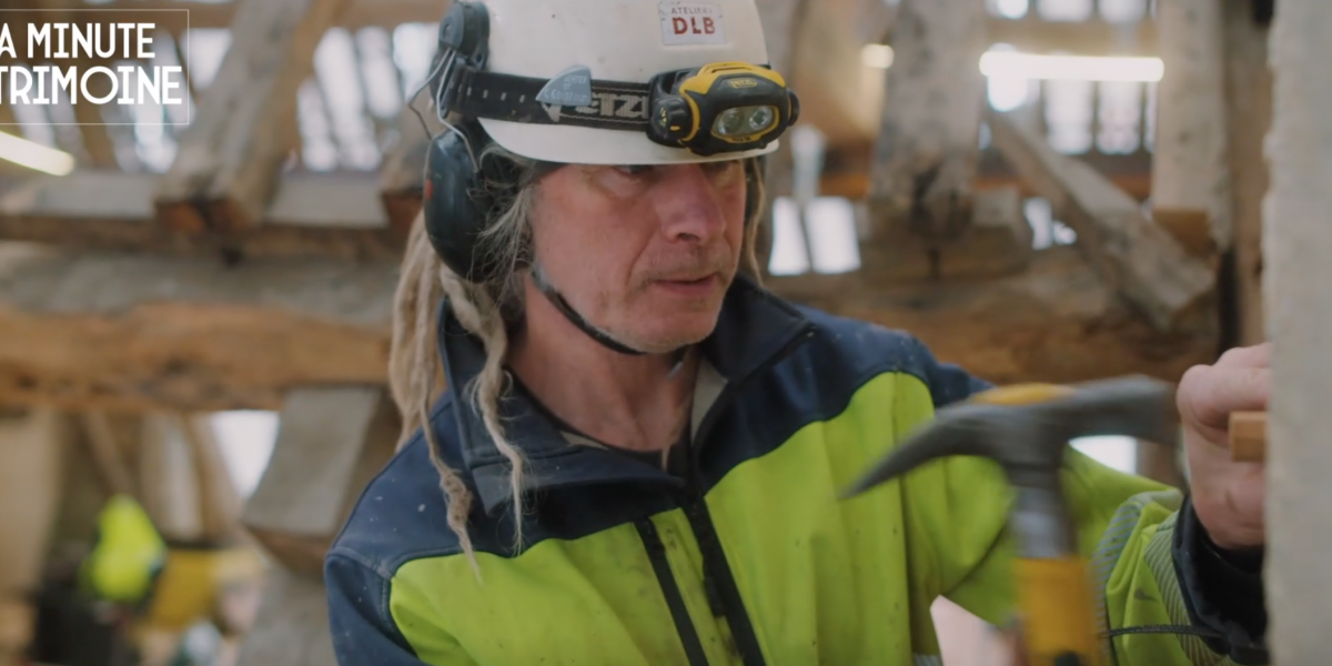 Charpentier travaillant sur une charpente en bois traditionnelle.